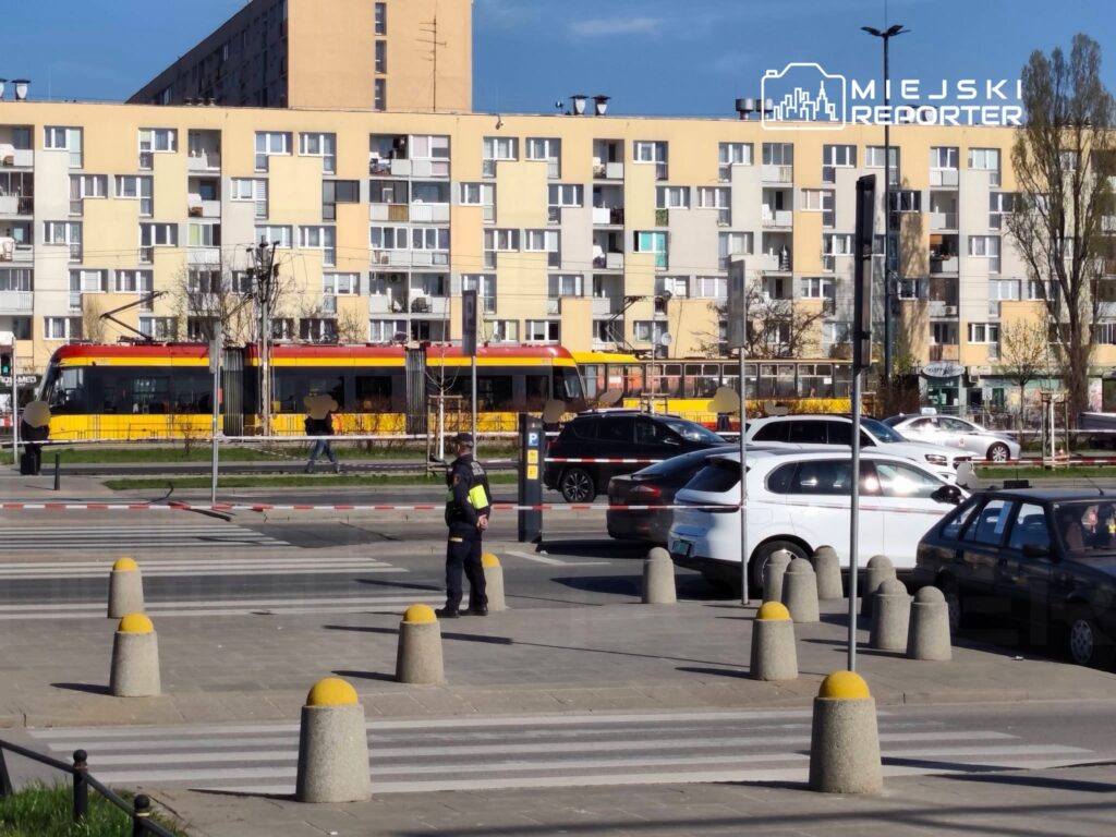 Policjant kierujący ruchem na przejściu dla pieszych obok przystanku tramwajowego w miejskim otoczeniu.