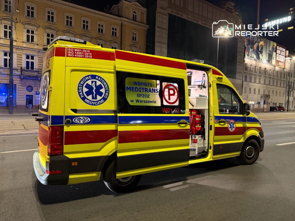 Karetka pogotowia z otwartymi drzwiami na oświetlonej ulicy w nocy, z widocznym logo Państwowego Ratownictwa Medycznego.