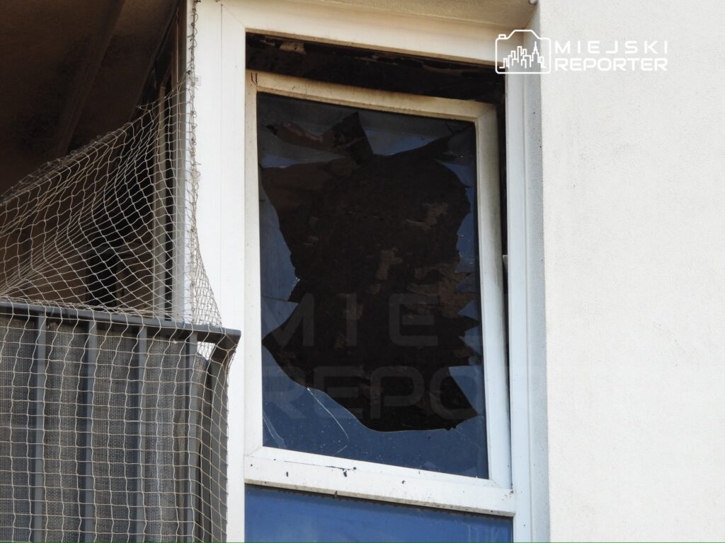 Zniszczona szyba okna w bloku mieszkalnym, z widocznym uszkodzeniem i zabrudzeniami na framudze.