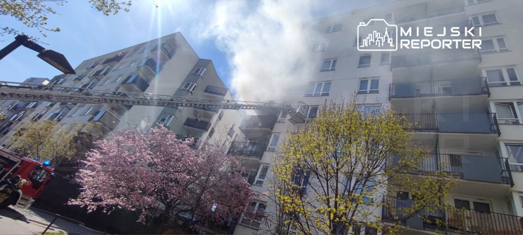 Drużyna strażaków korzysta z drabiny, gasząc pożar na wyższych piętrach nowoczesnego budynku mieszkalnego.