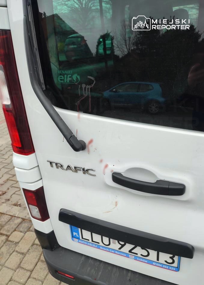 Zadrapania i plamy na tylnej klapie białego pojazdu dostawczego marki Renault Trafic zaparkowanego na chodniku.