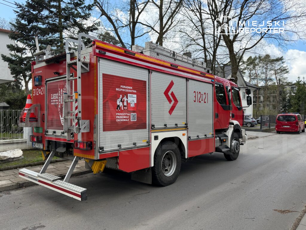 Czerwony wóz strażacki zaparkowany na ulicy, z widocznym numerem 31221 i oznaczeniem "Poradnik bezpieczeństwa".