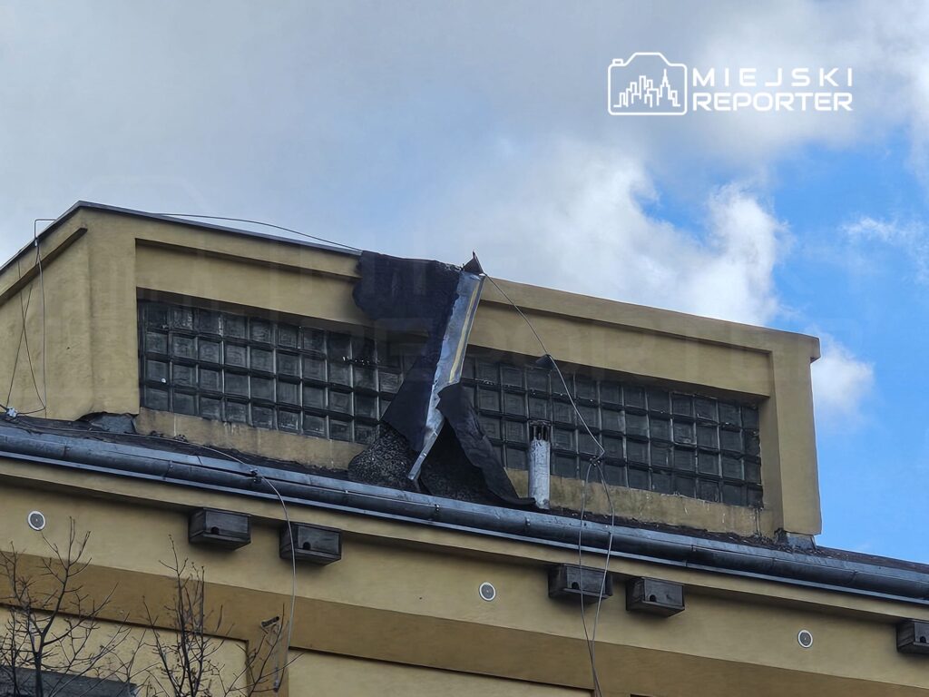 Uszkodzona część dachu budynku z widocznymi szczelinami i odstającymi fragmentami pokrycia.