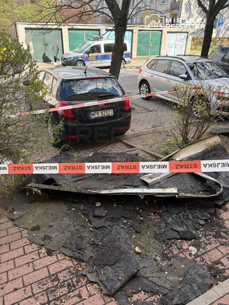 Czarny samochód zaparkowany obok uszkodzonej nawierzchni, otoczony taśmą policyjną w miejskim otoczeniu.
