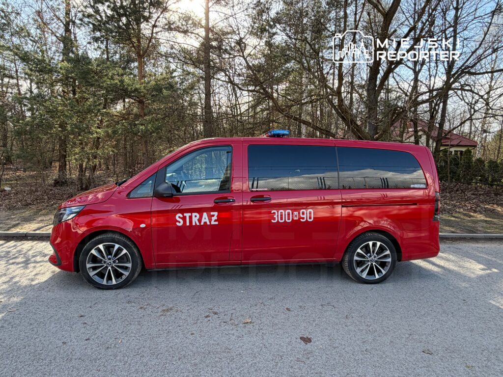 Czerwony samochód strażacki z napisem "STRAŻ" i numerem "300-90" zaparkowany na leśnej drodze.