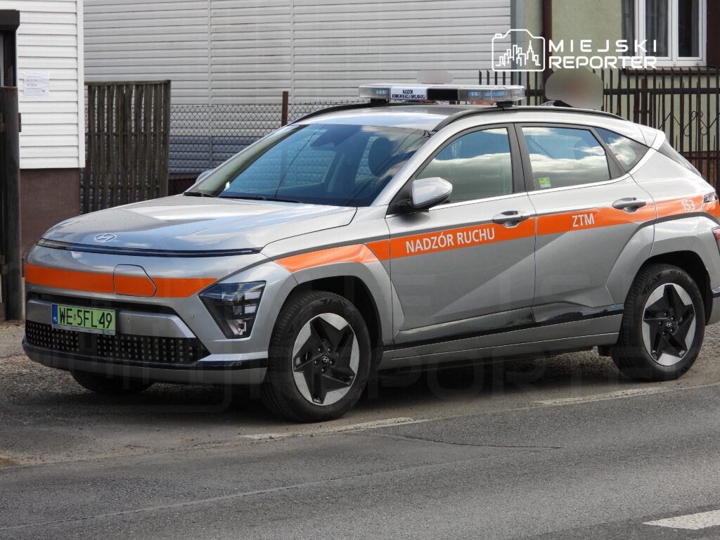 Samochód służbowy z oznaczeniem "Nadzór Ruchu ZTM" zaparkowany na ulicy, obok budynku mieszkalnego.