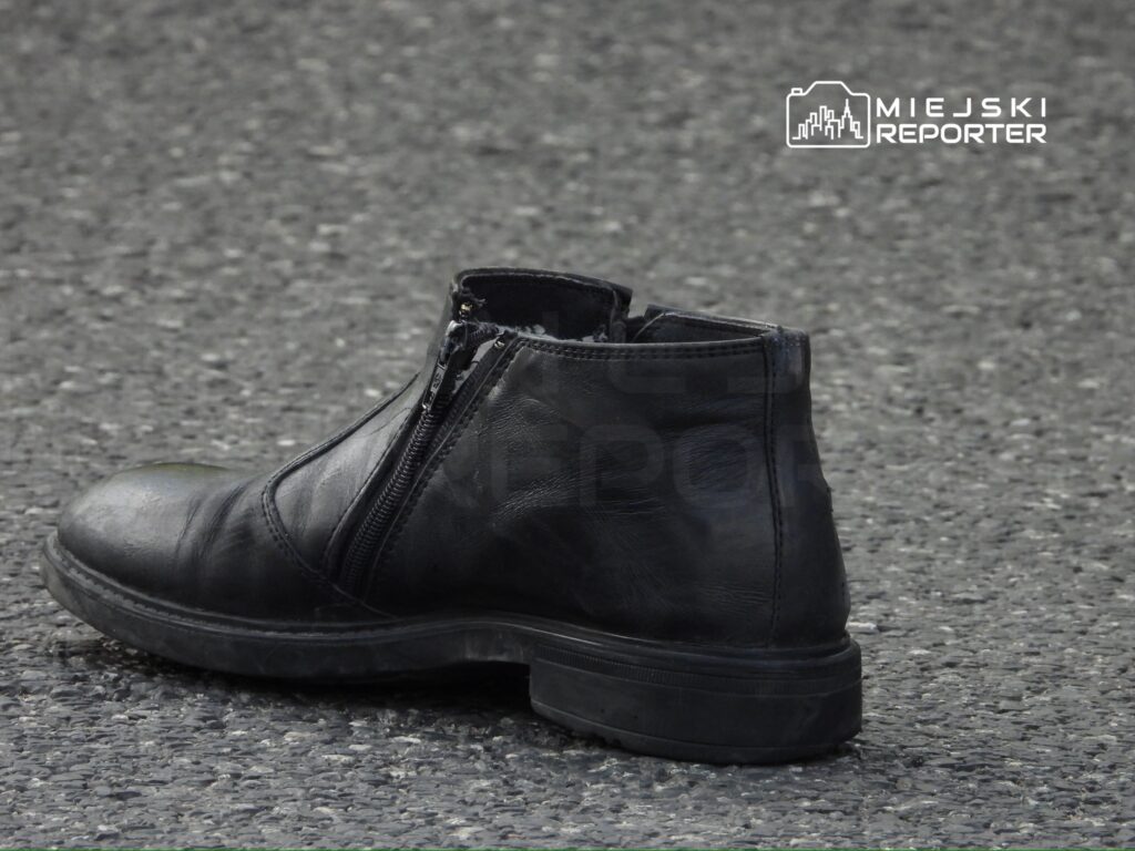 Czarny skórzany but z zamkiem błyskawicznym leży na szarej, asfaltowej nawierzchni.