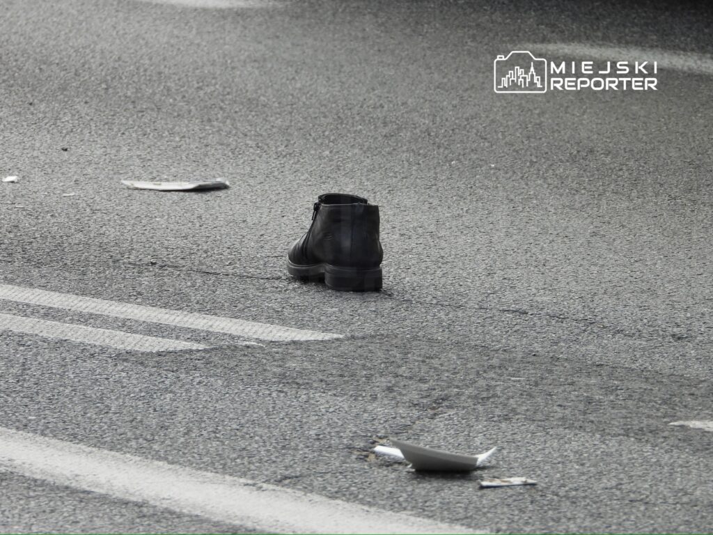 Czarny but umieszczony na szarej nawierzchni ulicy, obok porozrzucane kartki papieru.