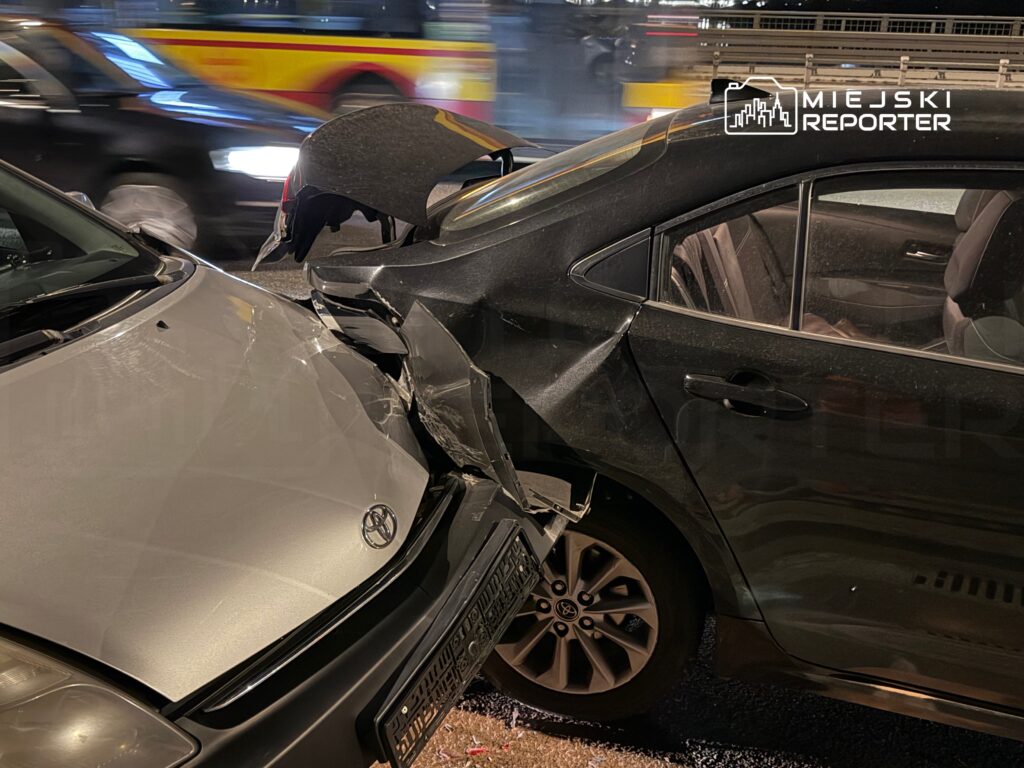 Dwa uszkodzone samochody po kolizji na ruchliwej ulicy, widoczne zarysowania na karoserii.