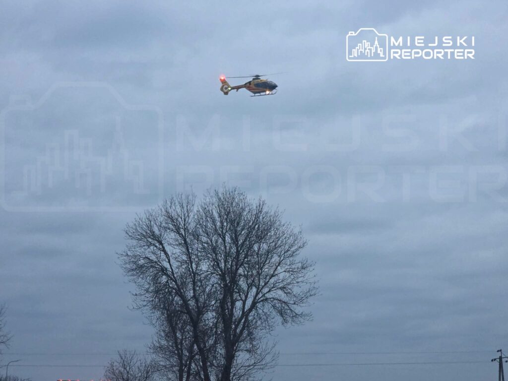 Śmigłowiec ratunkowy unosi się nad drzewami w pochmurnym niebie.