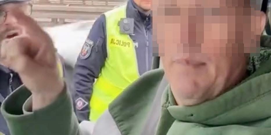 Mężczyzna w zielonej bluzie gestykuluje, rozmawiając z policjantami w mundurach na drodze.