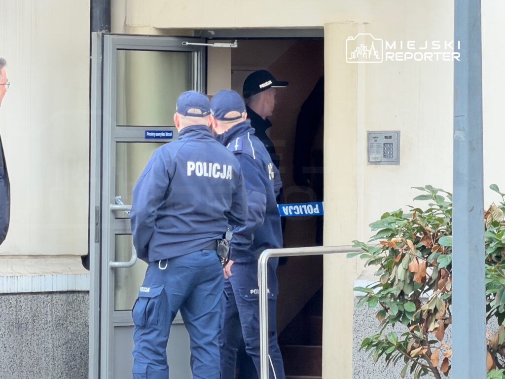 Grupa policjantów w mundurach stoi przed otwartymi drzwiami budynku, przygotowując się do wejścia.