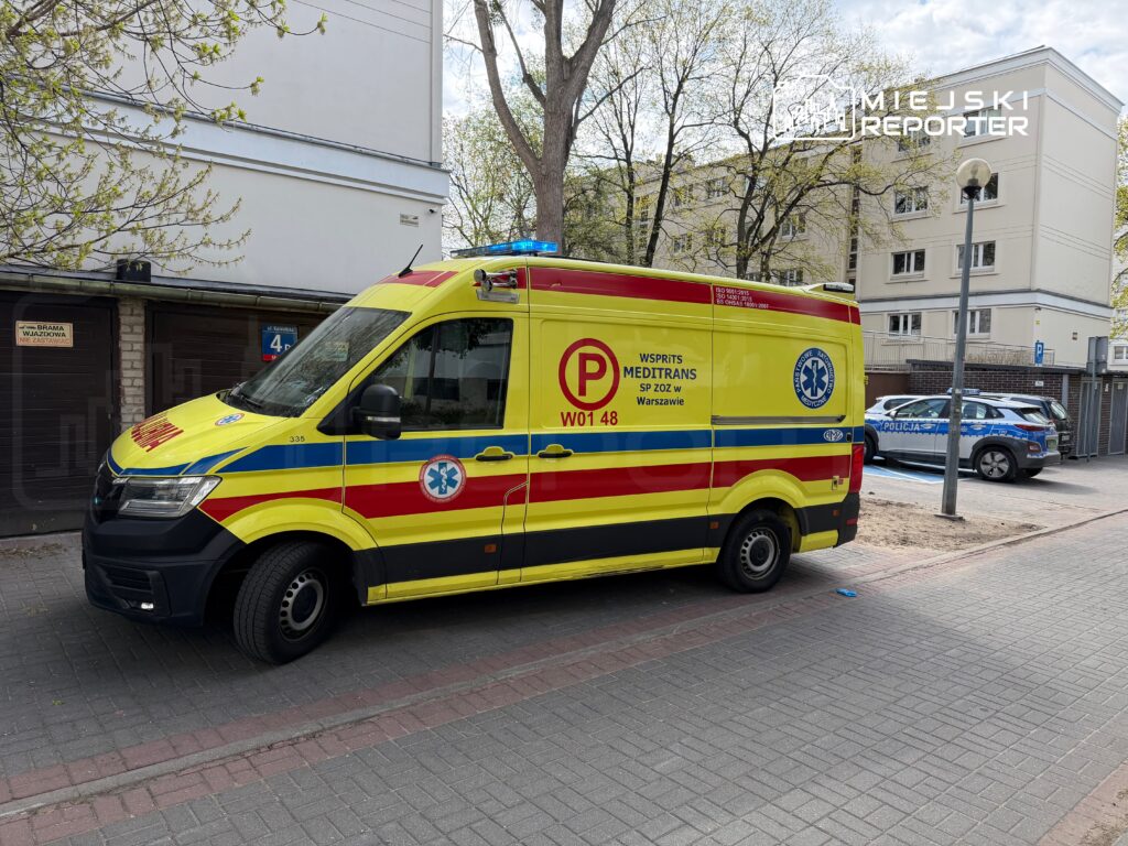 Karetka pogotowia w żółto-czerwonych barwach stojąca na ulicy obok budynku mieszkalnego.