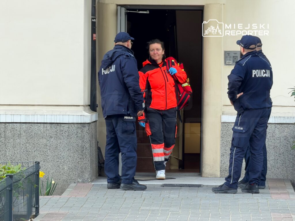 Kobieta w odzieży ratunkowej wychodzi z budynku, rozmawiając z dwoma policjantami w mundurach.