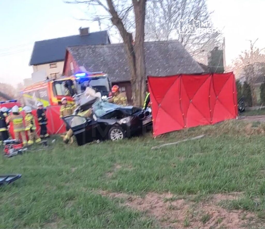 Ratownicy medyczni udzielają pomocy poszkodowanym w wypadku drogowym obok rozbitego samochodu na trawie.
