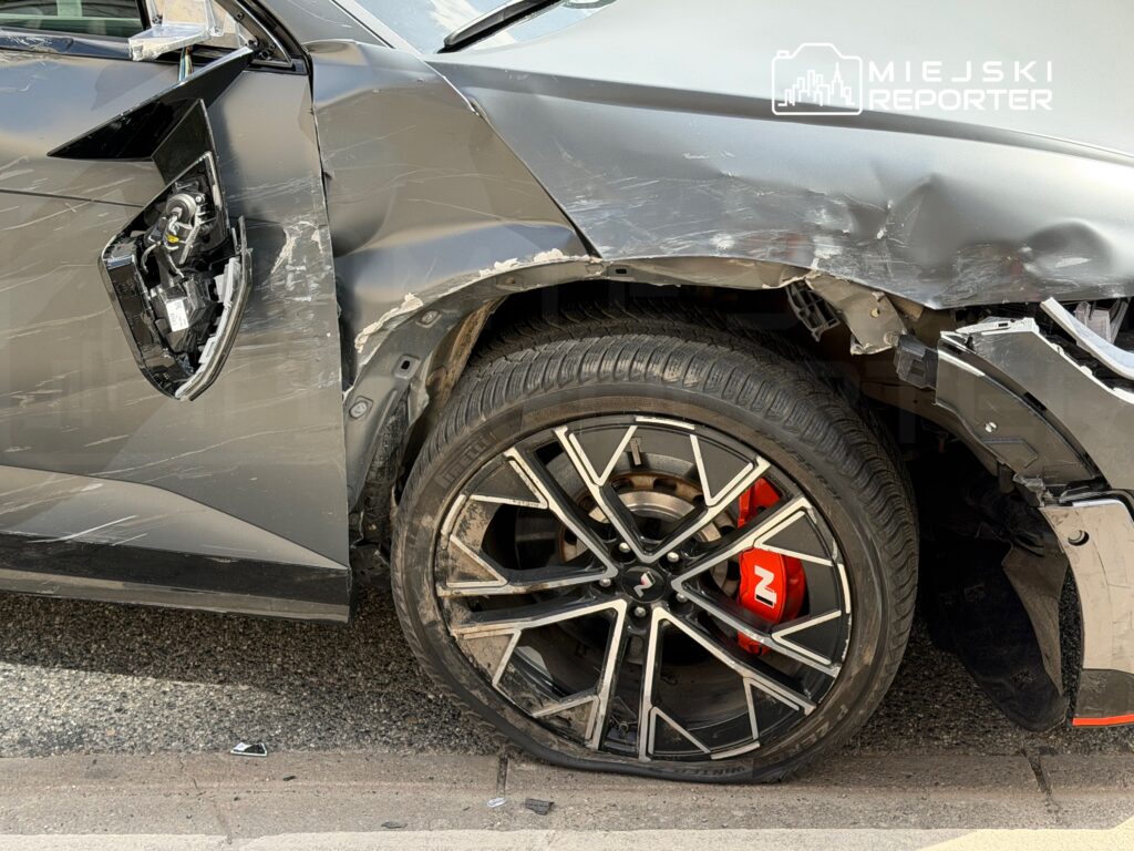 Uszkodzony samochód osobowy z porysowanym nadwoziem i zniszczonym błotnikiem, stojący na ulicy.