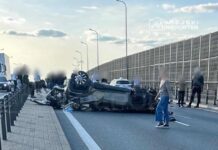 Na pasie ruchu leży przewrócone auto, a wokół zgromadziło się kilka osób obserwujących zdarzenie.