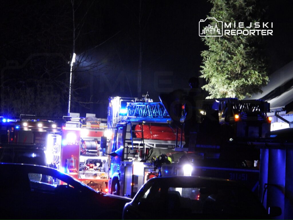 Strażacy pracują przy wozie strażackim z włączonymi sygnalizacjami świetlnymi w nocy.