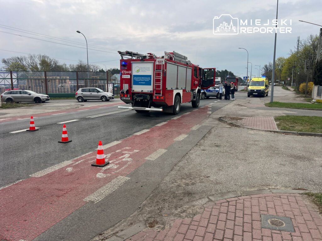 Na jezdni stoją samochody straży pożarnej i karetka, a wokół ustawione są pachołki drogowe.