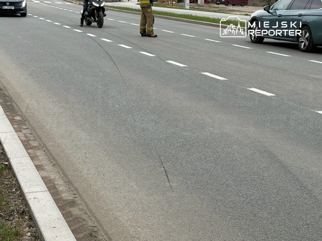 Motocyklista zatrzymany na jezdni obok oznakowanego miejsca zdarzenia, obok niego stoi policjant.