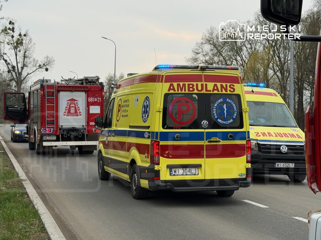 Karetkę pogotowia i wóz strażacki zatrzymane na drodze, obok pojazdów cywilnych na pasie ruchu.