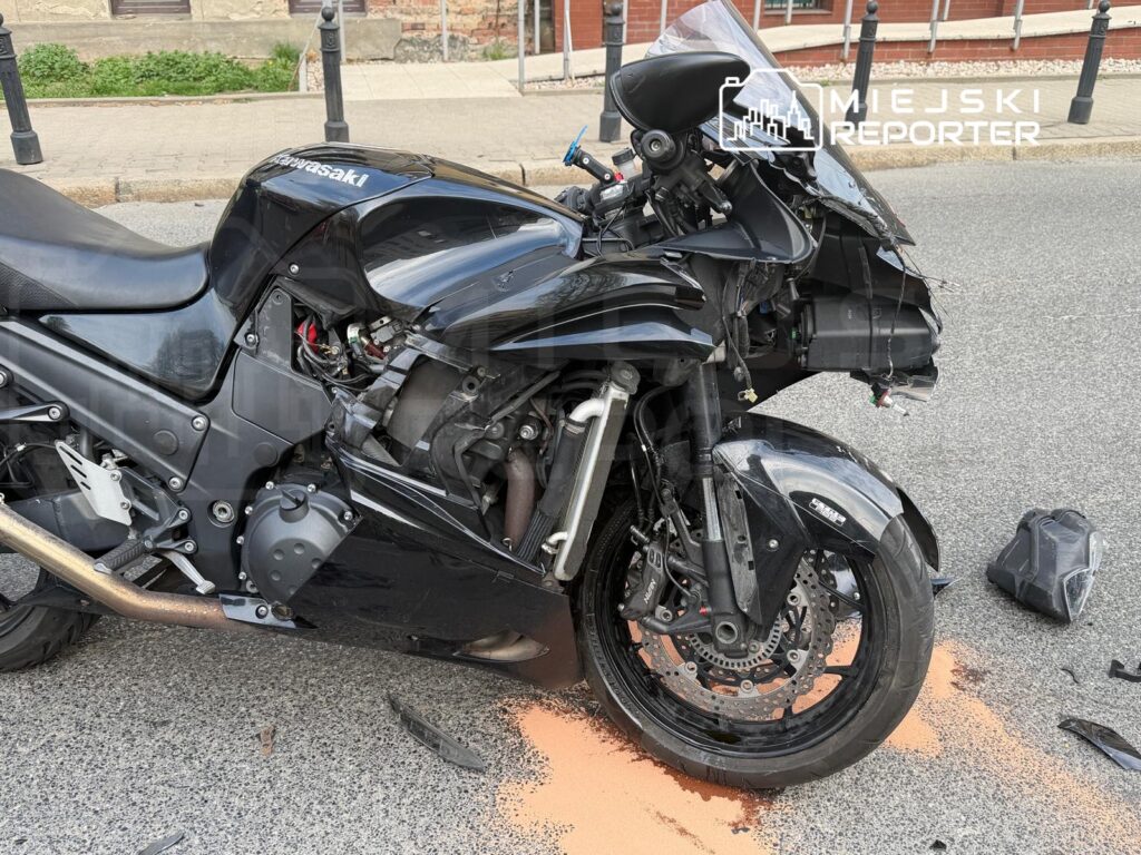 Uszkodzony motocykl typu sportowego leży na drodze, wokół niego widać fragmenty plastików i plamę oleju.