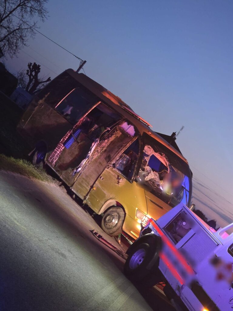 Zniszczony autobus stoi na drodze, obok niego znajduje się pojazd służb ratunkowych z włączonymi sygnałami świetlnymi.