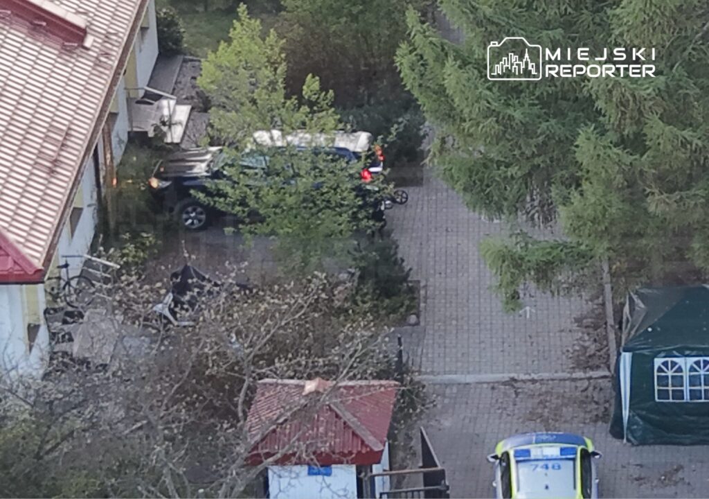 Czarny SUV zaparkowany przed budynkiem mieszkalnym, w otoczeniu zieleni i sprzętu ogrodowego.