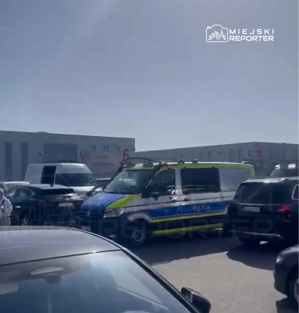 Policyjny radiowóz zaparkowany w zatłoczonym parkingu, otoczony przez inne samochody.