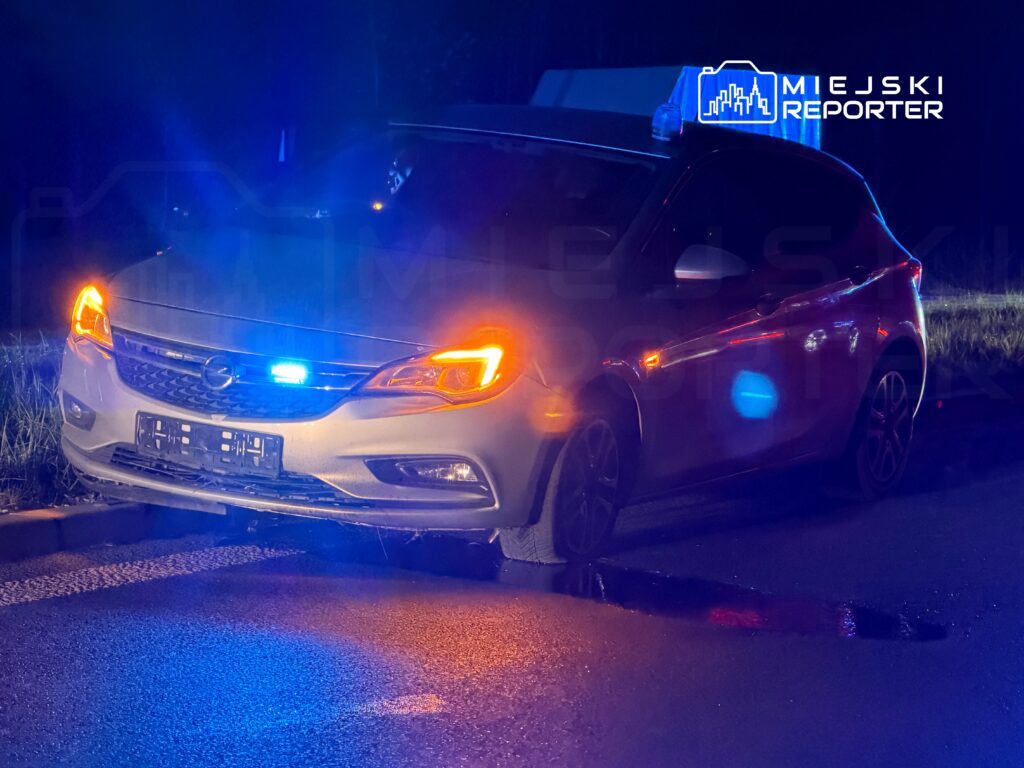 Radiowóz policyjny z niebieskimi i pomarańczowymi światłami stojący na drodze w nocy.