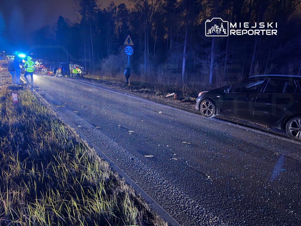 Na drodze nocą, z niebieskimi światłami, ratownicy udzielają pomocy poszkodowanym w wypadku samochodowym.