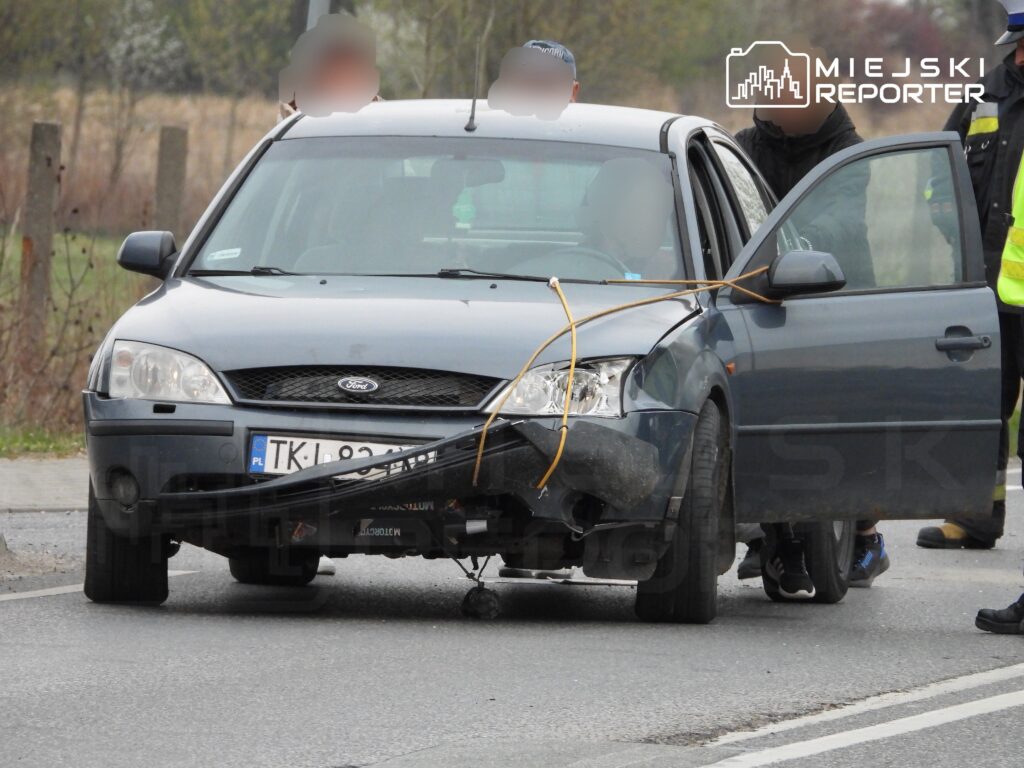 Uszkodzony niebieski samochód osobowy stoi na drodze, z otwartymi drzwiami i unieruchomioną przednią częścią.