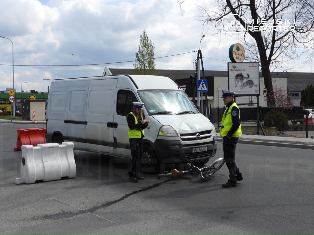 Funkcjonariusze policji kontrolują miejsce zdarzenia drogowego z udziałem białego furgonu i roweru.