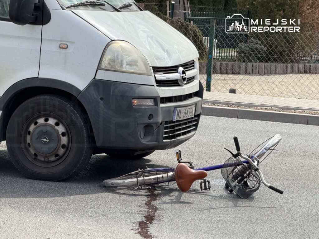 Biały furgon stoi obok przewróconego roweru na drodze, obok widoczna plama czerwonej cieczy.