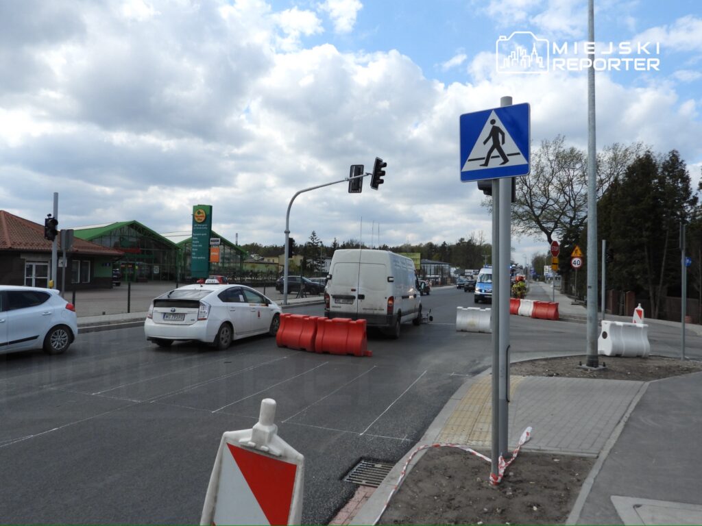 Ruch samochodowy zatrzymany przy sygnalizacji świetlnej na drodze z barierkami drogowymi w tle.