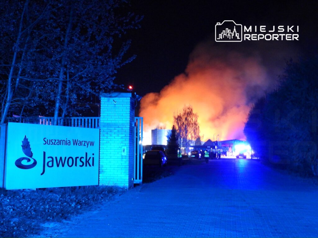 Pożar w suszarni warzyw Jaworski, intensywne płomienie i dym widoczne w nocy, w tle pojazdy straży pożarnej.