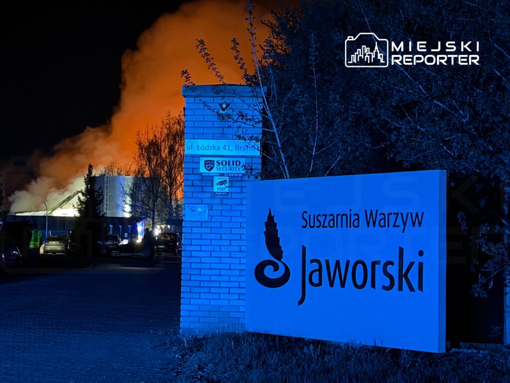 Pomarańczowy dym wydobywający się z budynku suszarni warzyw, w tle widoczne niebieskie światła i tablica z nazwą "Jaworski".