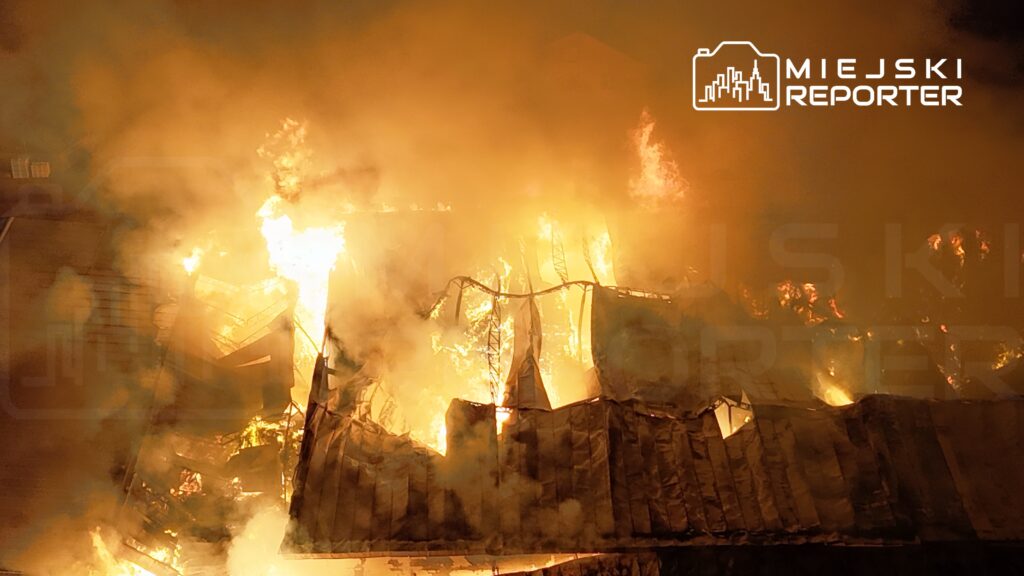 Intensywne płomienie i gęsty dym wydobywają się z zniszczonego budynku w nocy.