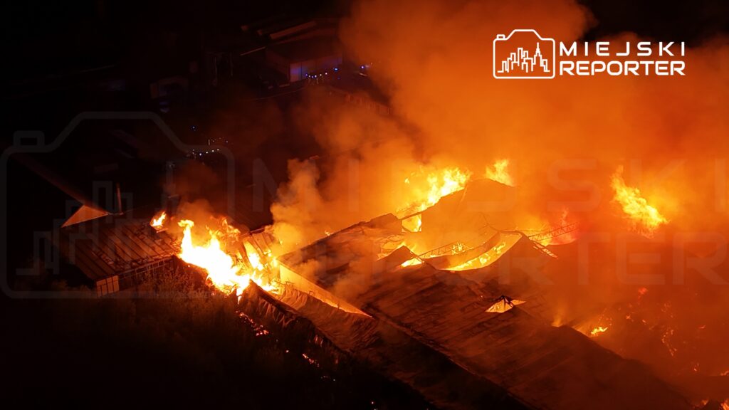 Pożar ogarnia dach budynku, emitując intensywne płomienie i dym w ciemnej nocy.