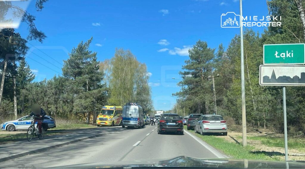 Ruch drogowy zatrzymany przy drodze, obok policyjny radiowóz i karetka, w tle znaki drogowe.