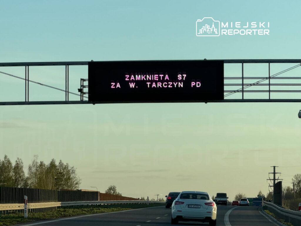 Elektroniczny znak drogowy informujący o zamknięciu S7 za W. Tarczyń PD, widok na ruchliwą drogę.
