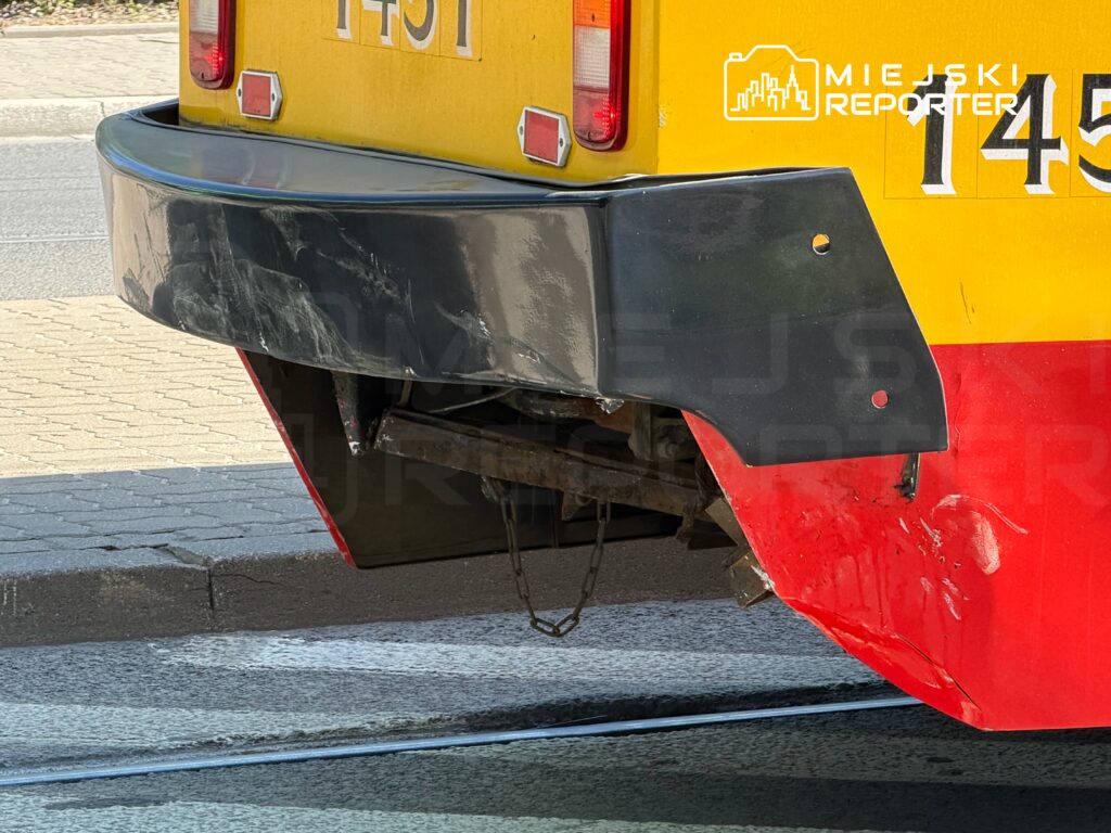 Zniszczony tył pojazdu szynowego z widocznymi zarysowaniami i uszkodzeniami w miejskim otoczeniu.