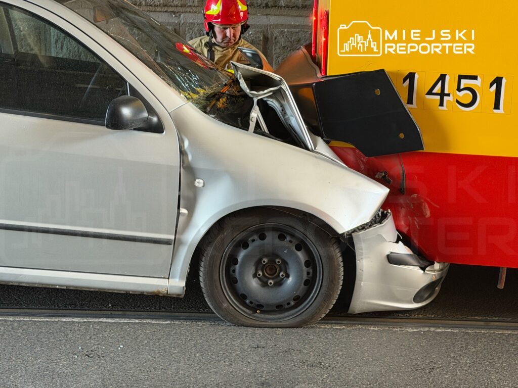 Kierowca w hełmie sprawdza uszkodzone auto osobowe zderzone z pojazdem służb ratunkowych na ulicy.