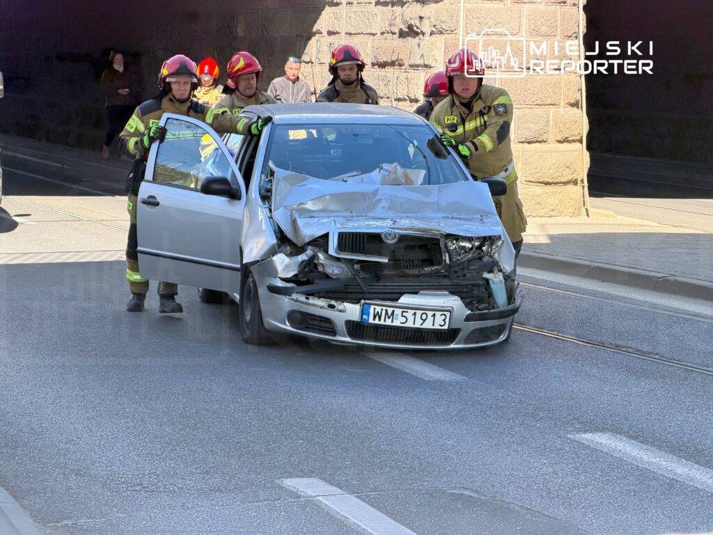 Strażacy usuwają poszkodowany samochód osobowy z uszkodzeniem przodu na miejskiej ulicy.
