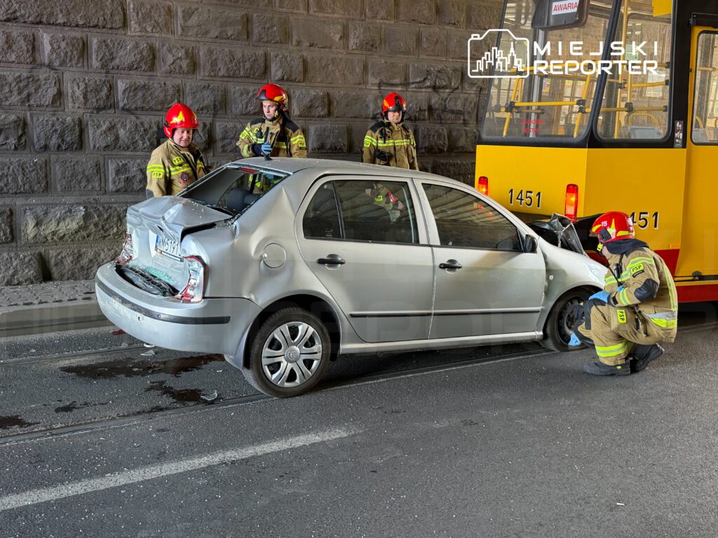Czterech strażaków ocenia uszkodzenia samochodu osobowego po kolizji z tramwajem w tunelu. W tle widać żółty tramwaj.