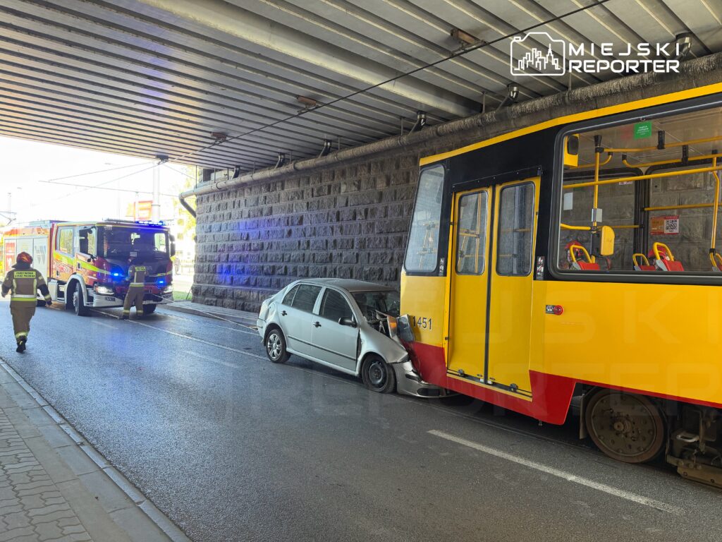 W miejscu zdarzenia strażacy pracują przy zderzeniu tramwaju z osobowym samochodem pod wiaduktem.