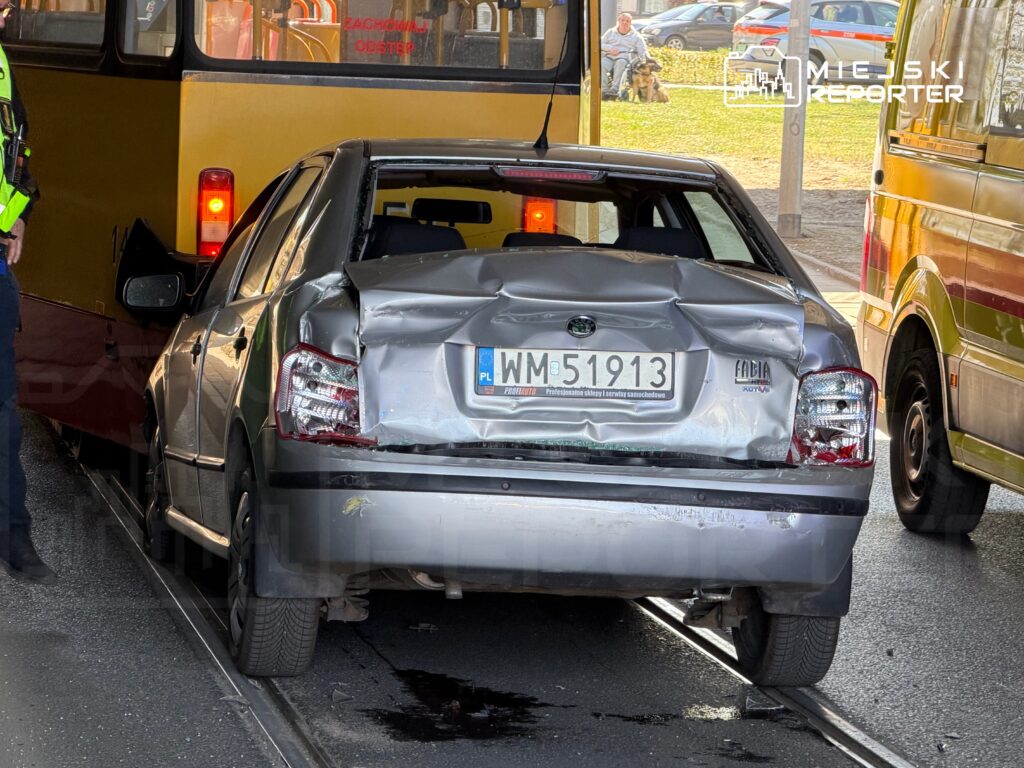 Uszkodzony samochód osobowy stoi na torowisku obok autobusu, a policjant rozmawia z kierowcą.
