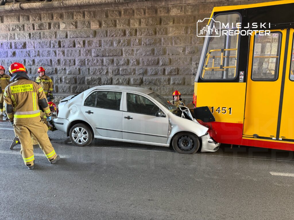 Kierowca samochodu osobowego zderza się z tramwajem pod wiaduktem, a strażacy udzielają pomocy.