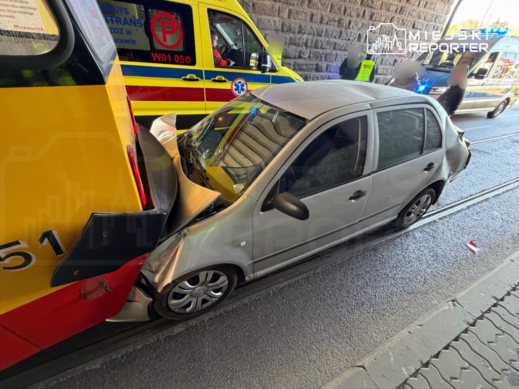 Zderzenie samochodu osobowego z tramwajem na ulicy, w tle widać pojazdy ratunkowe.