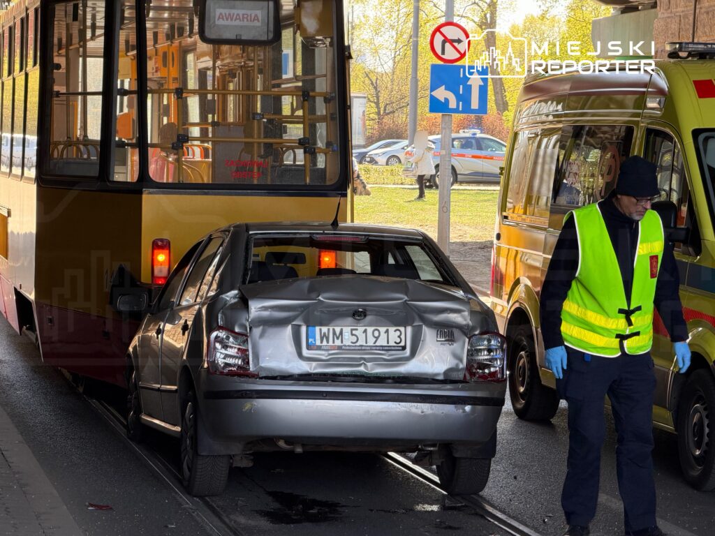 Wypadek komunikacyjny z udziałem tramwaju i uszkodzonego samochodu osobowego, obok pracownik służb ratunkowych.